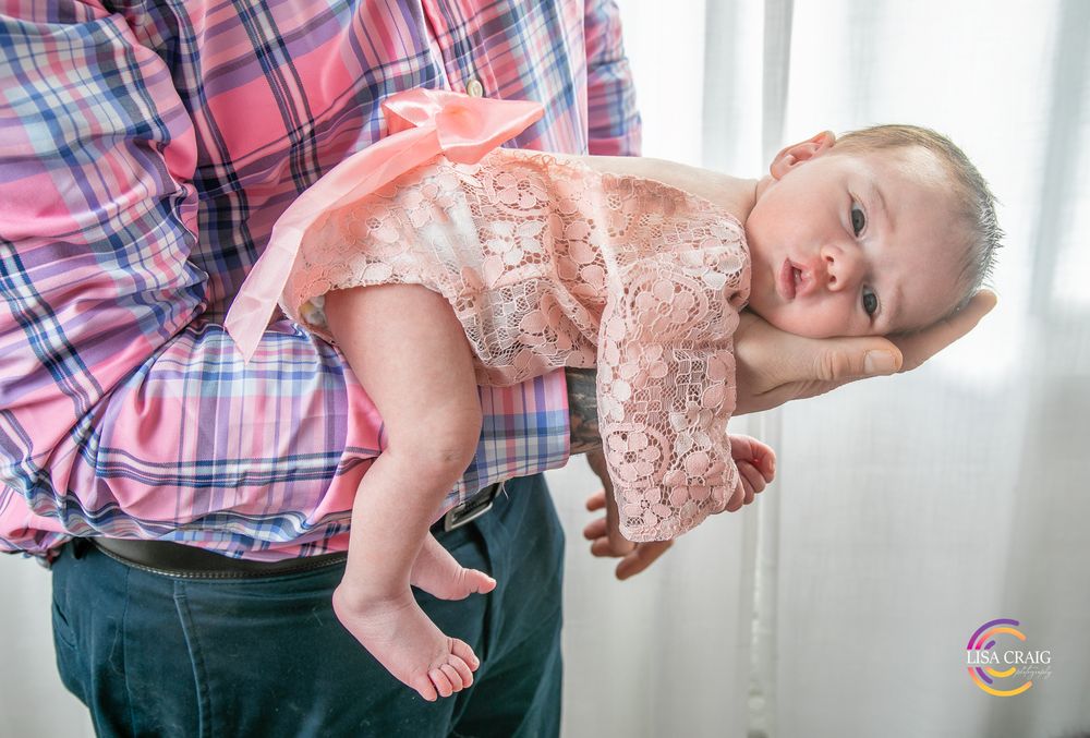Parent in plaid shirt holding a laughing baby in front of a white curtained window.