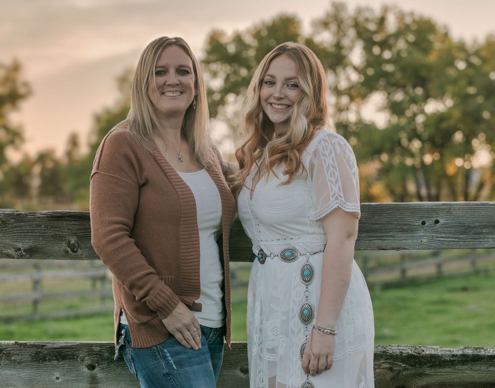 People in casual attire pose for outdoor photos in a grassy countryside setting during golden hour sunset.