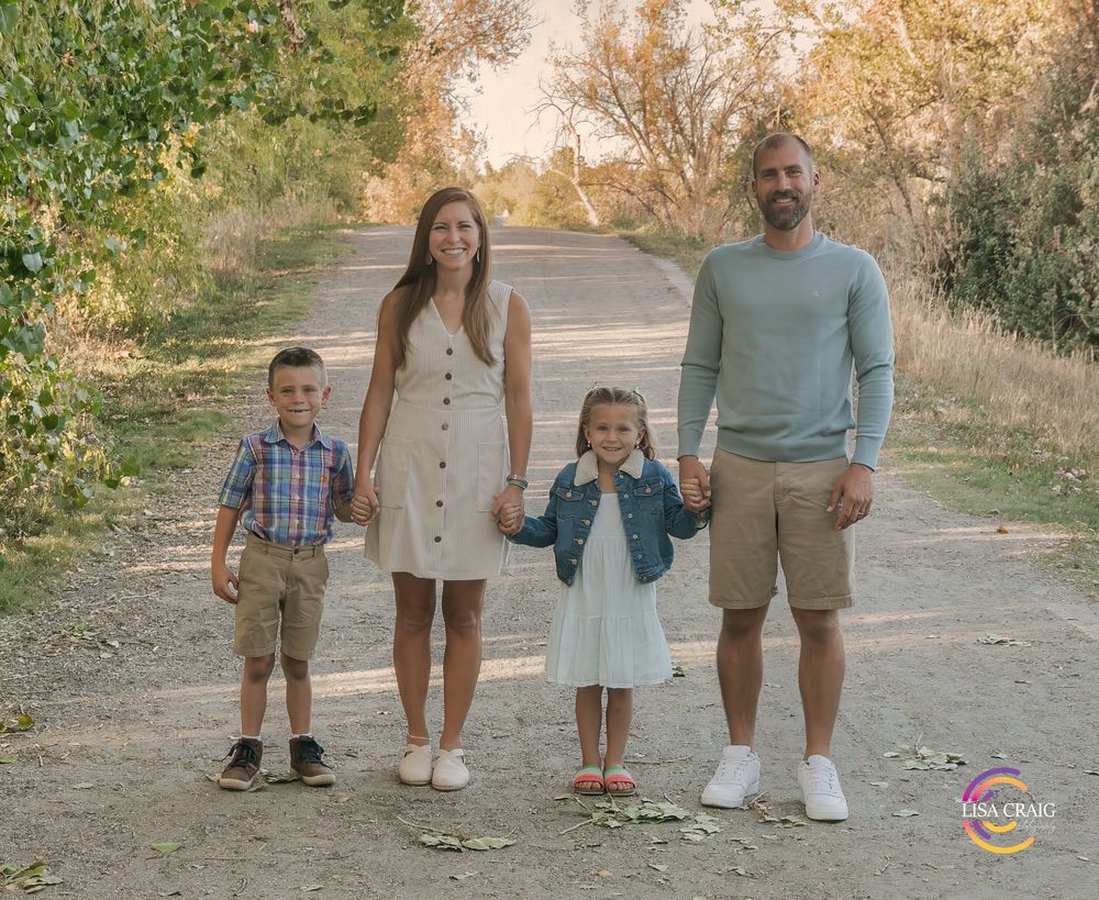 A casual gathering of people standing together on a dirt path with natural foliage in the background during sunset.