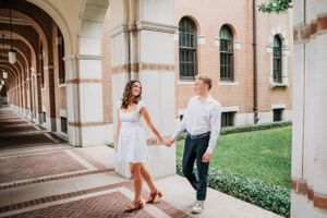 A couple walking hand in hand along an arched colonnade corridor next to a manicured lawn.