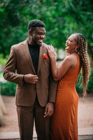 Joyful couple sharing a candid laughing moment together outdoors, with her wearing orange and him in a brown suit.
