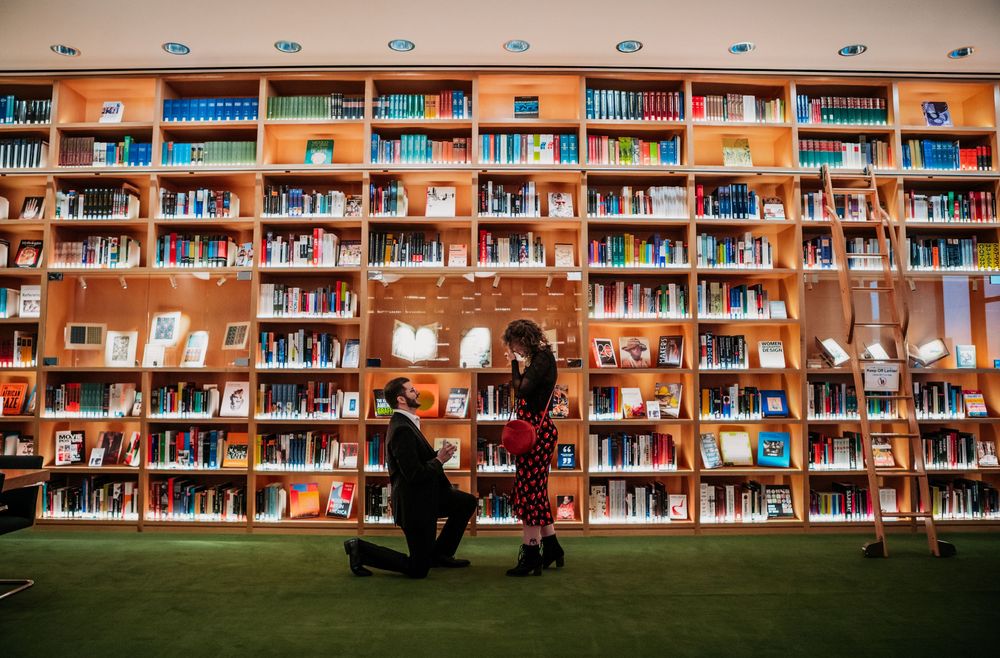 A panoramic view of a library interior with rows of bookshelves filled with colorful books and study spaces. Proposal. Engagement