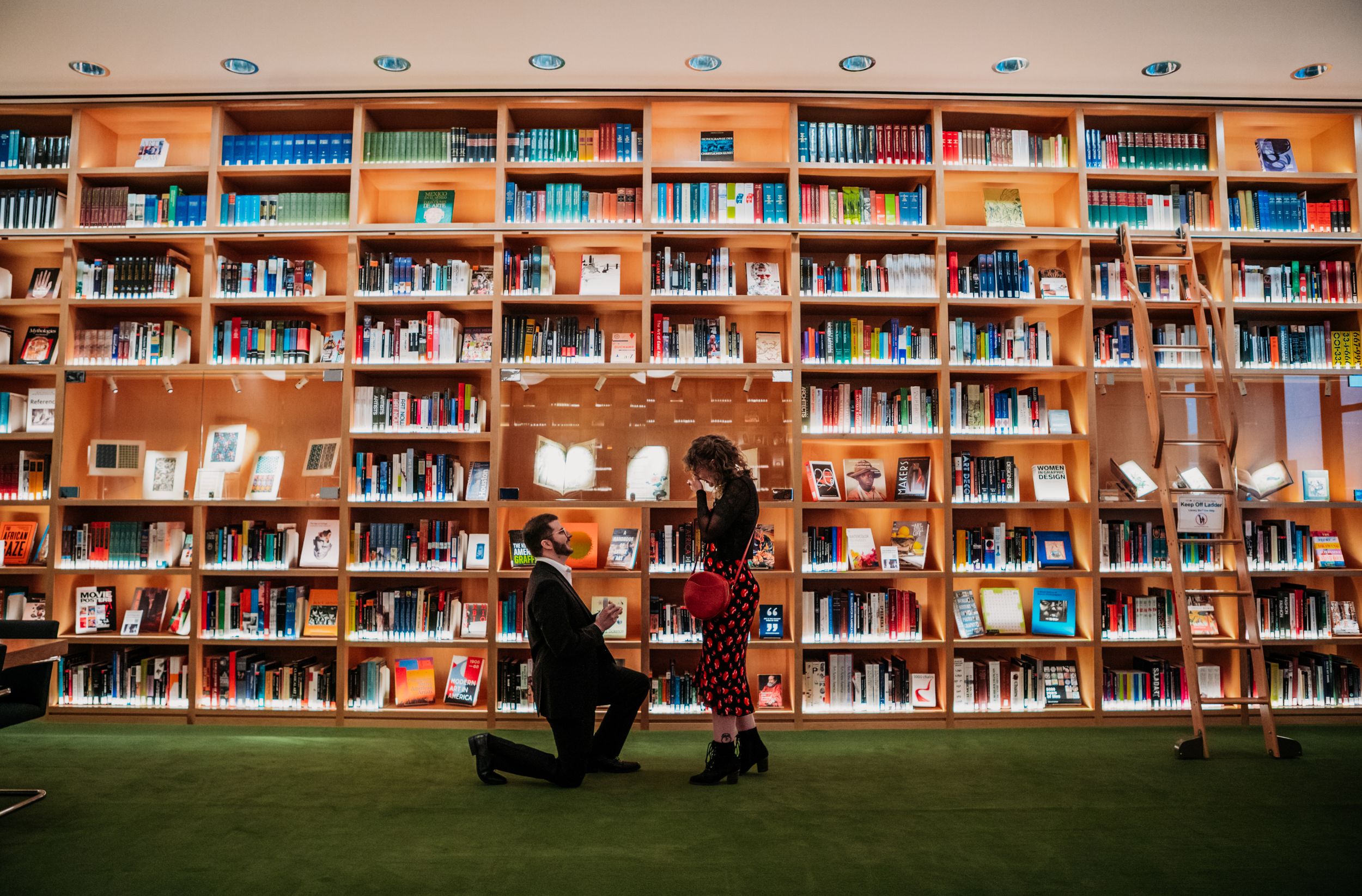 A panoramic view of a library interior with rows of bookshelves filled with colorful books and study spaces. Proposal. Engagement