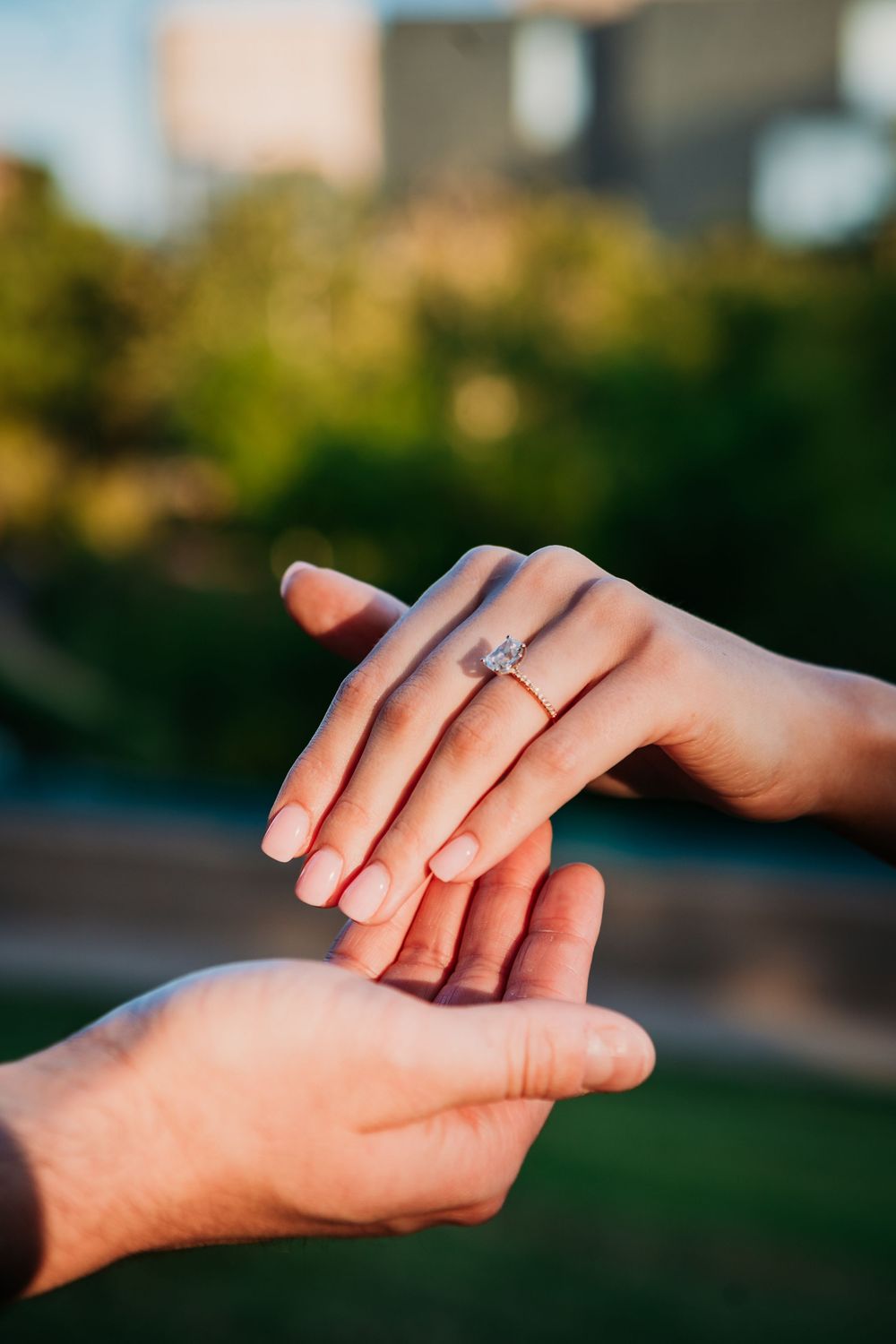 Close-up of hands showing off an engagement ring with a diamond solitaire in warm sunset lighting outdoors.