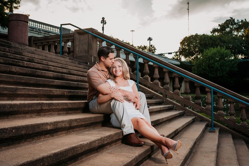 A couple shares an intimate moment while sitting on historic stone steps with ornate railings at dusk. Engagement