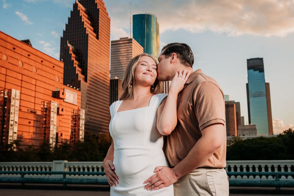 A couple shares an intimate moment against a backdrop of modern city buildings during golden hour sunset. Engagement