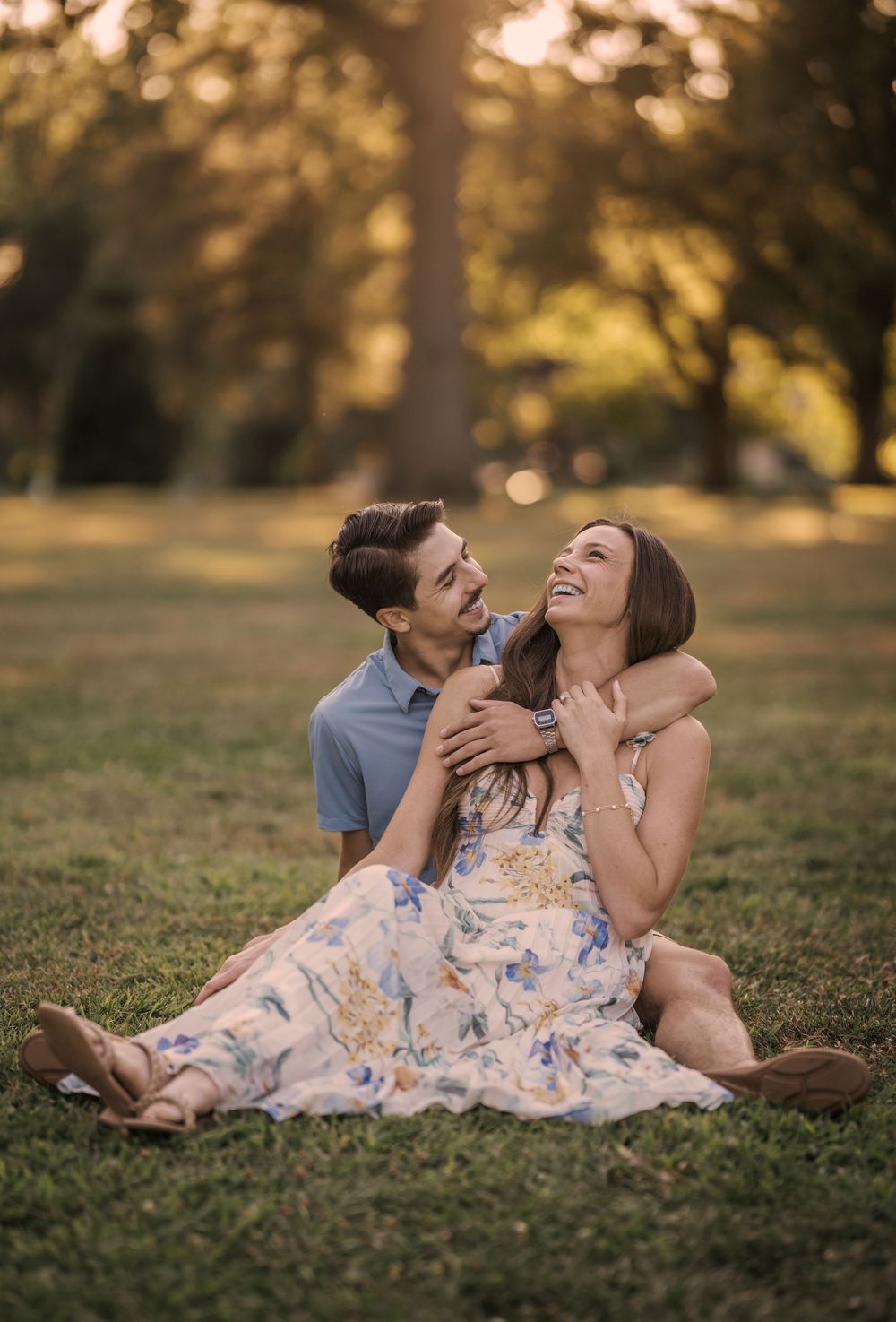 A couple lying together on grass during golden hour sharing intimate laughter and joyful moments in a park setting.
