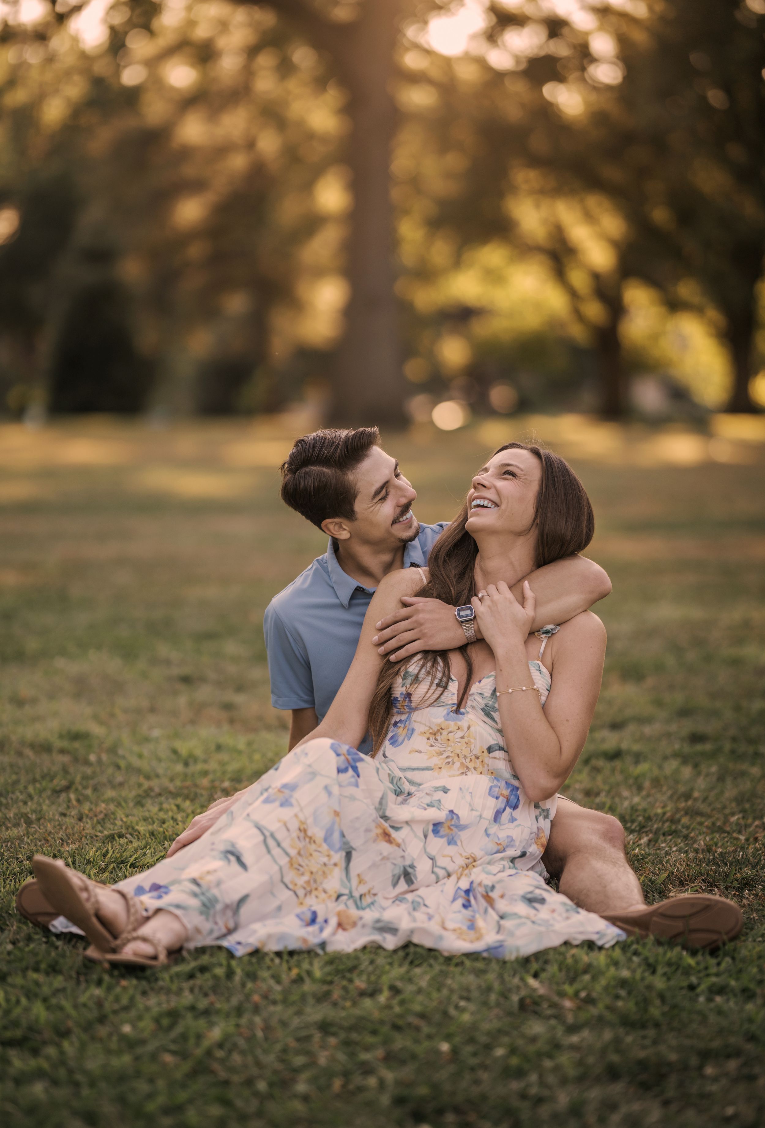 A couple lying together on grass during golden hour sharing intimate laughter and joyful moments in a park setting.