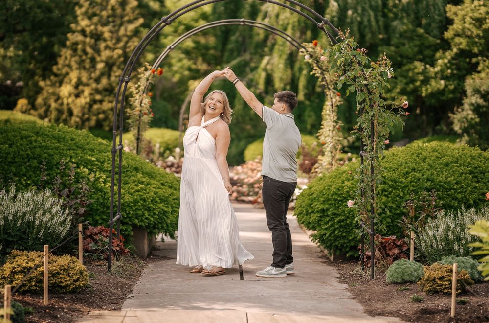 A couple dances together on a winding garden path surrounded by lush greenery and blooming flowers.