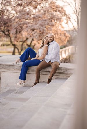 A couple sits together on concrete steps during sunset with autumn trees creating a romantic backdrop.