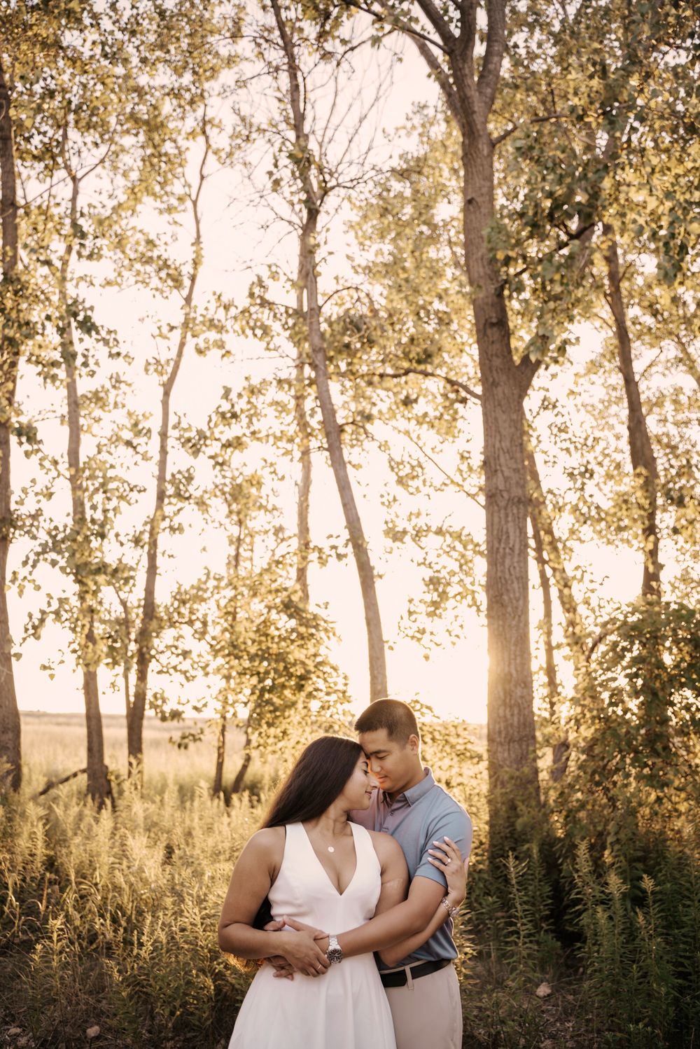 Romantic couple embraces in a sunlit forest during golden hour with trees creating a dreamy backdrop.