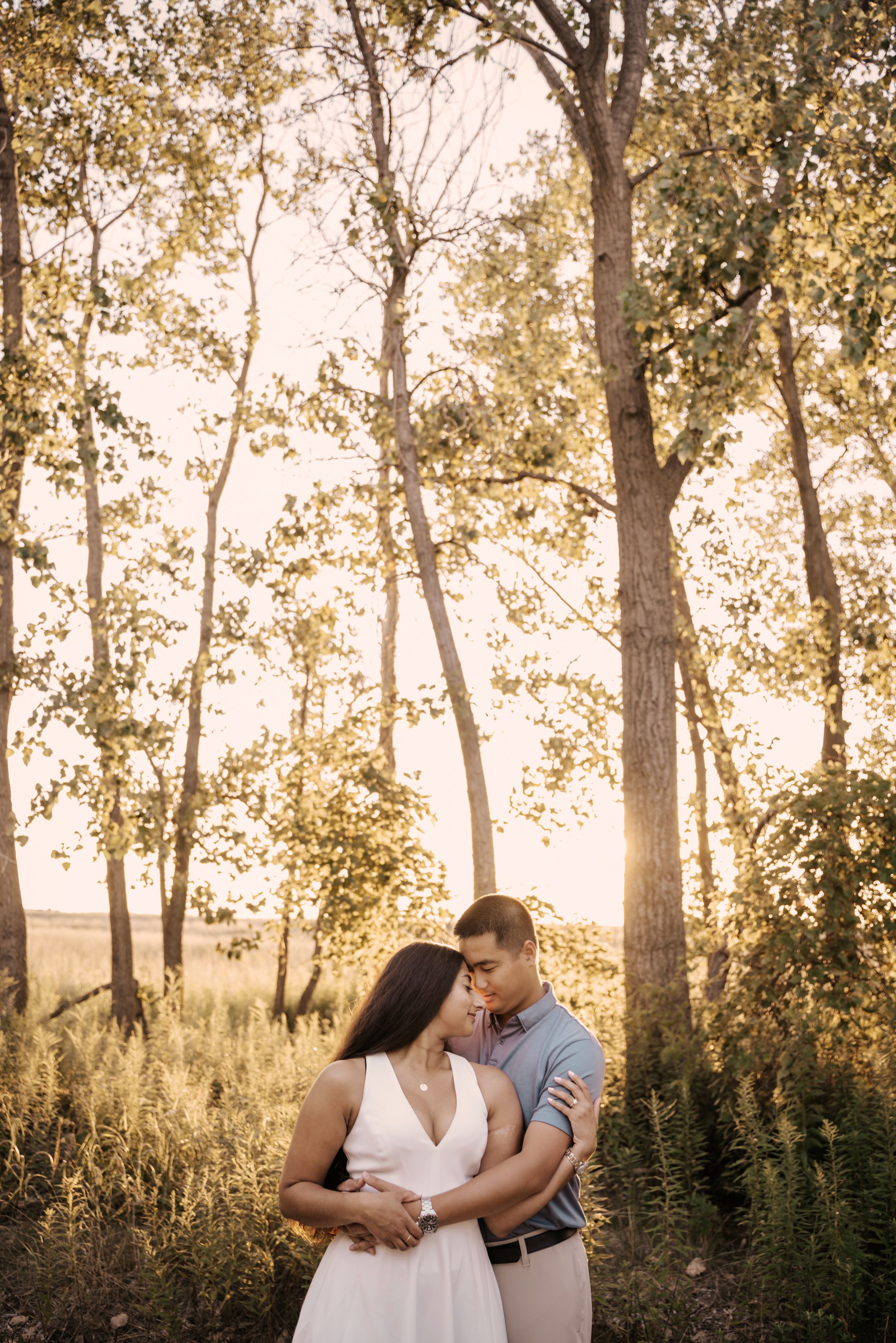 Romantic couple embraces in a sunlit forest during golden hour with trees creating a dreamy backdrop.
