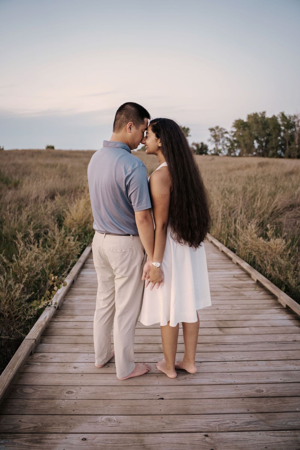Couple sitting together on a wooden boardwalk through a serene grassland at sunset.