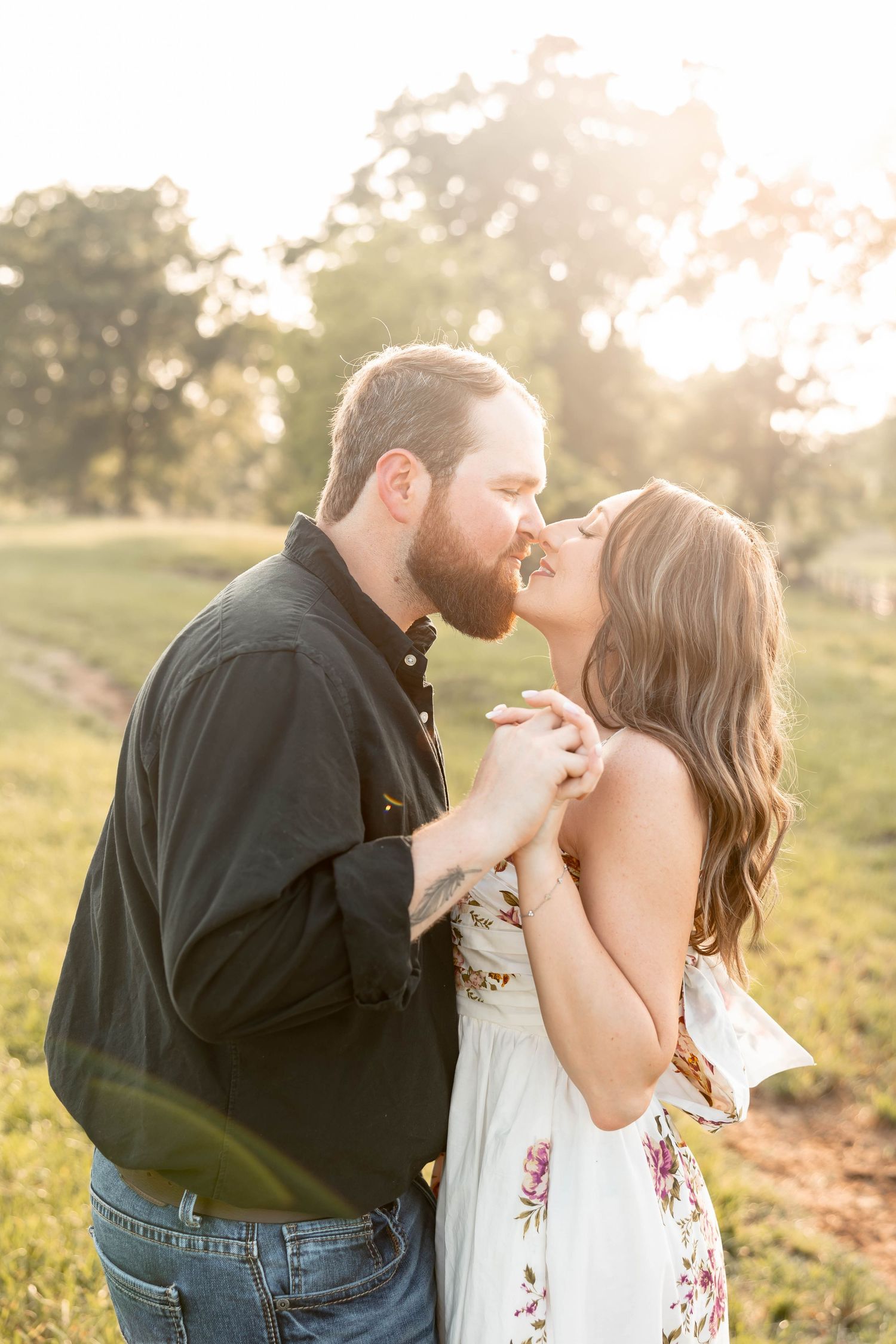 Playful couple performs lifting poses in grassy field at sunset.