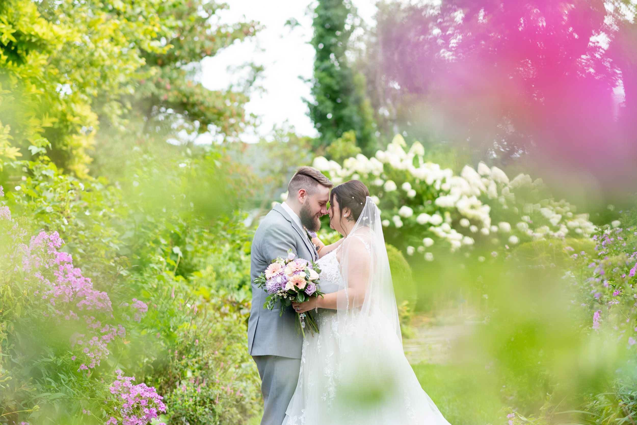 Wedding portraits in a lush garden with pink and white flowers blooming at Mac Cuddy Botanic Garden