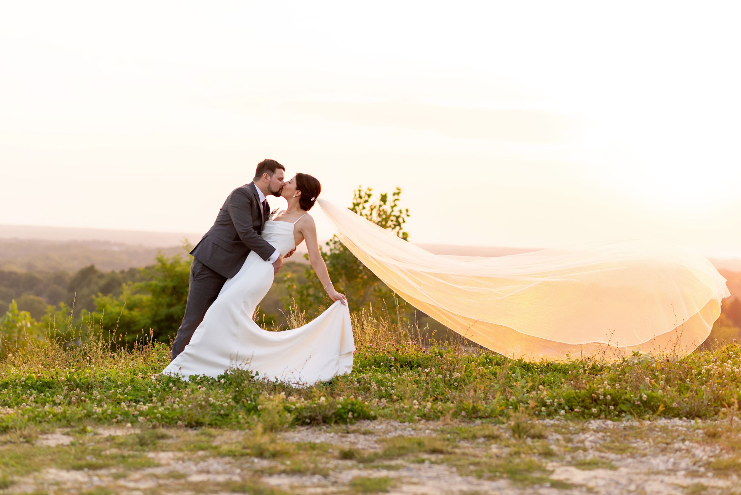 Romantic wedding photo series with a flowing veil at sunset in a meadow.