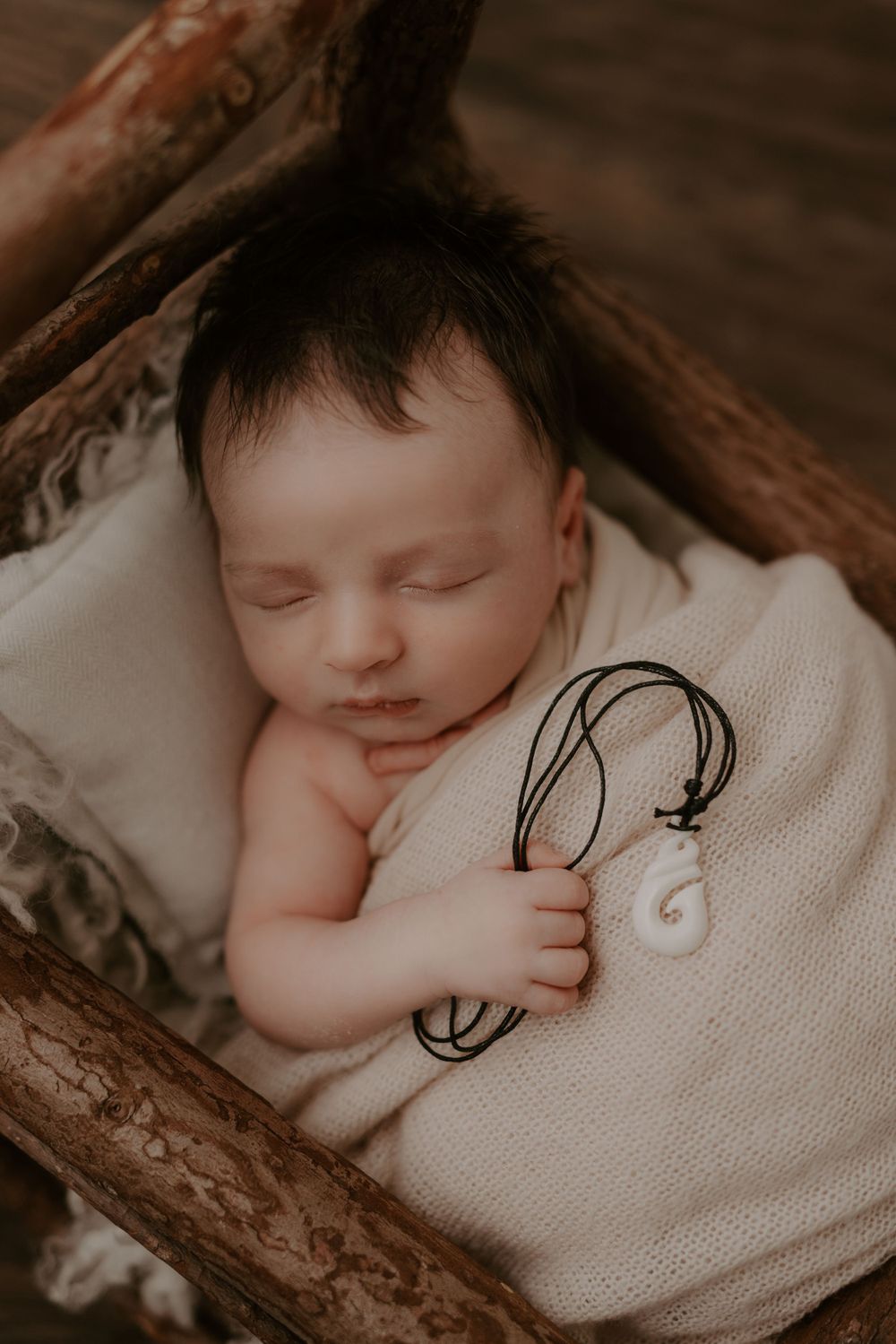 Sleeping newborn wrapped in cream blanket on rustic wooden surface.