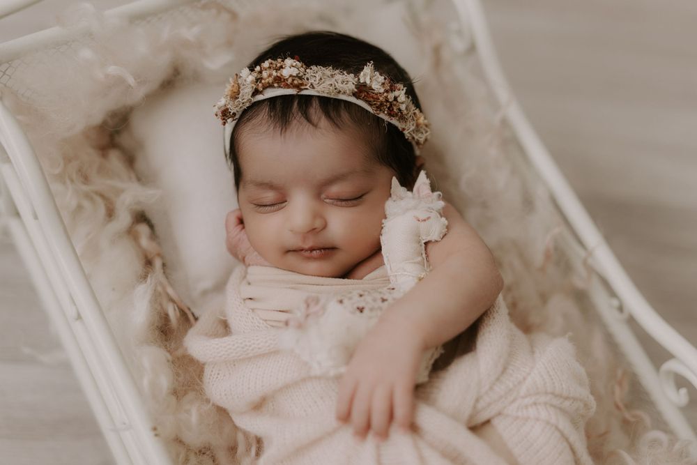 Peaceful newborn sleeping in vintage bassinet with lace details and floral crown.