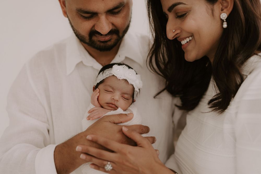 Intimate family portrait series showing tender moments with a newborn baby in white tones.