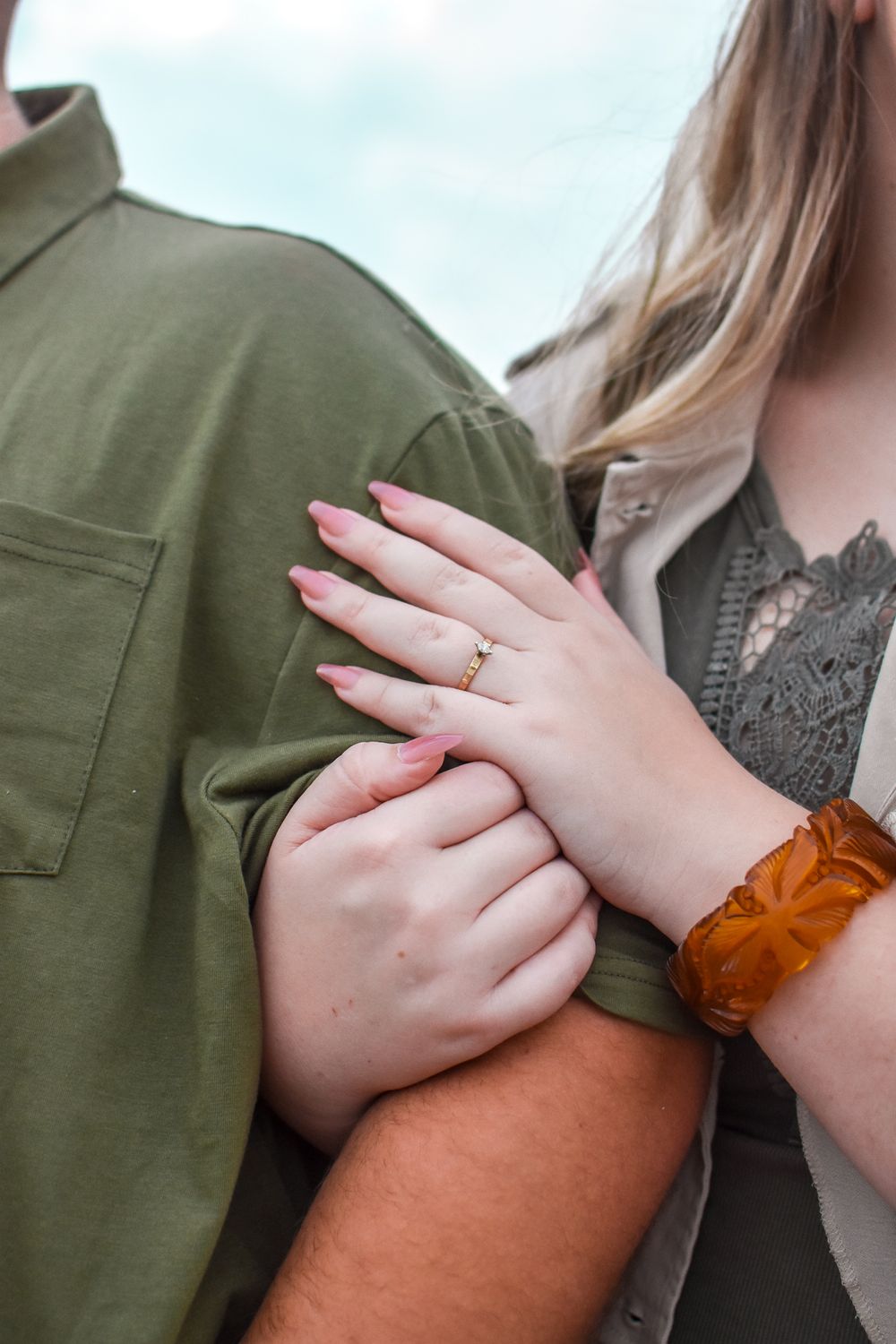 A close-up of hands showing off a new engagement ring against an olive green jacket background.
