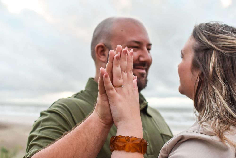 Two people share an intimate moment together on a cloudy beach as one tenderly touches the other's face.