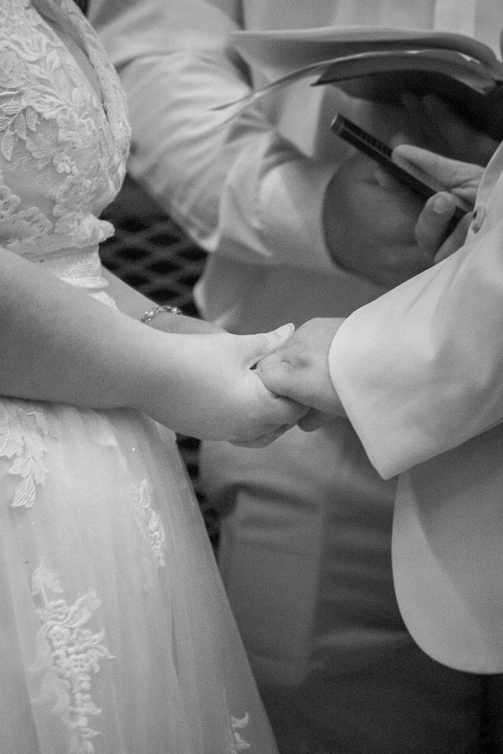 A black and white image capturing a close-up of hands during a wedding ceremony.