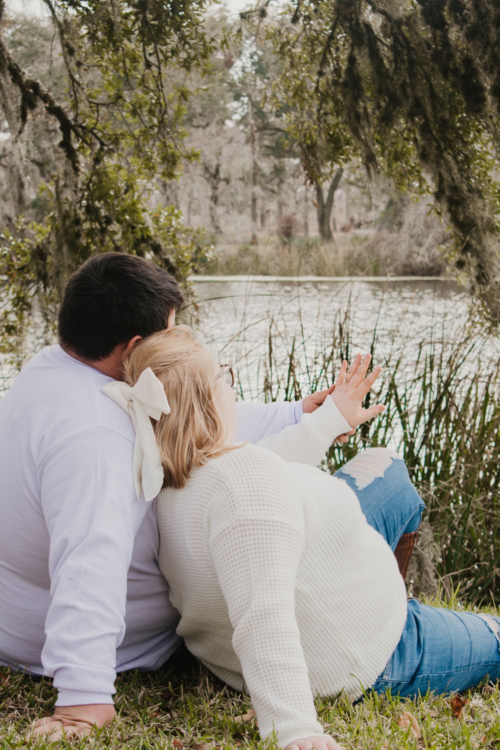 Couple relaxing together by a peaceful pond with Spanish moss hanging from trees in the background.
