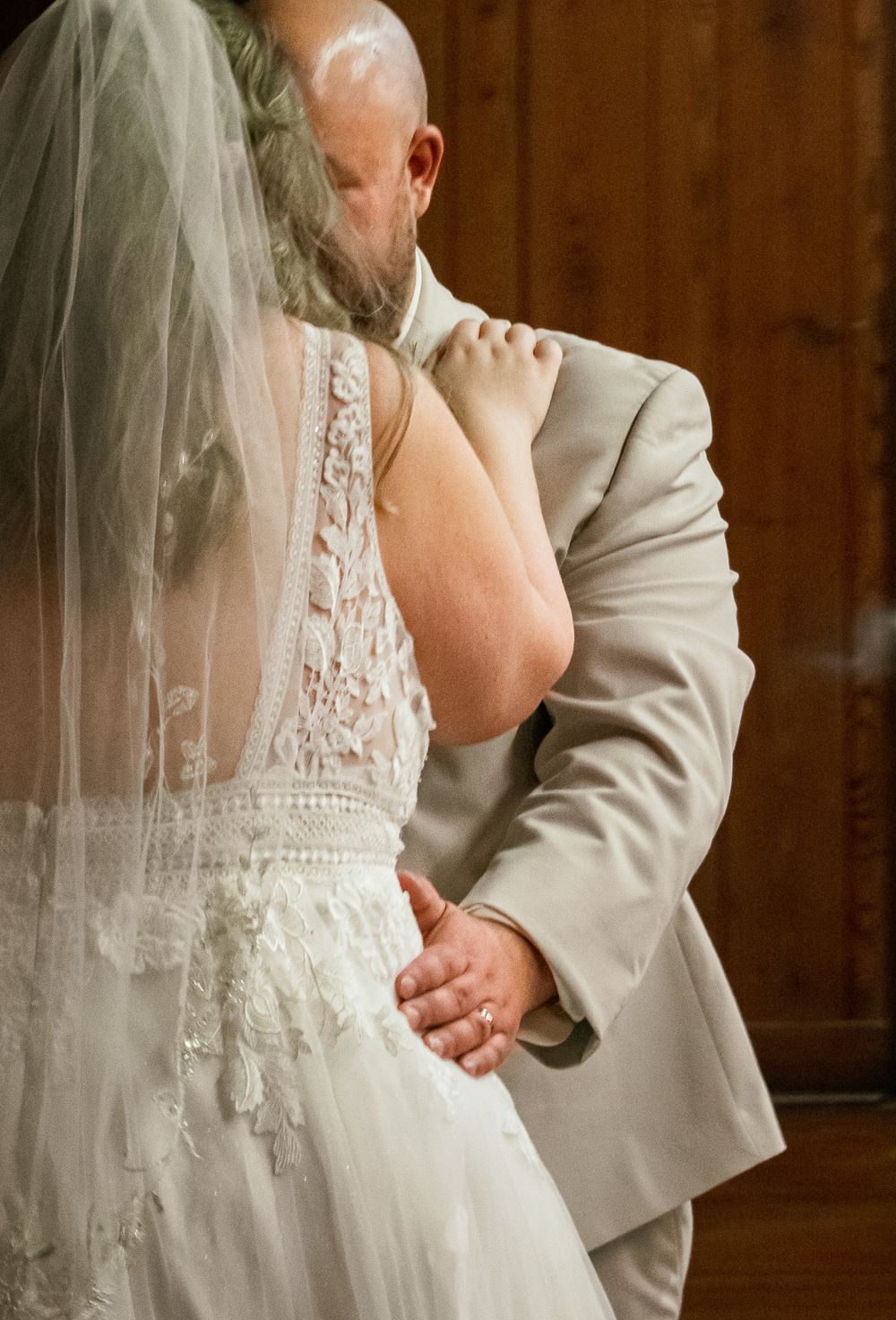 A tender moment captured during a wedding dance showing the intricate lace details of a white bridal gown and gray suit.