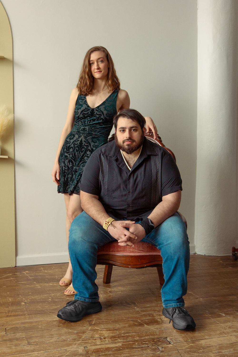 Portrait of two people in casual attire posing together near a white column indoors.