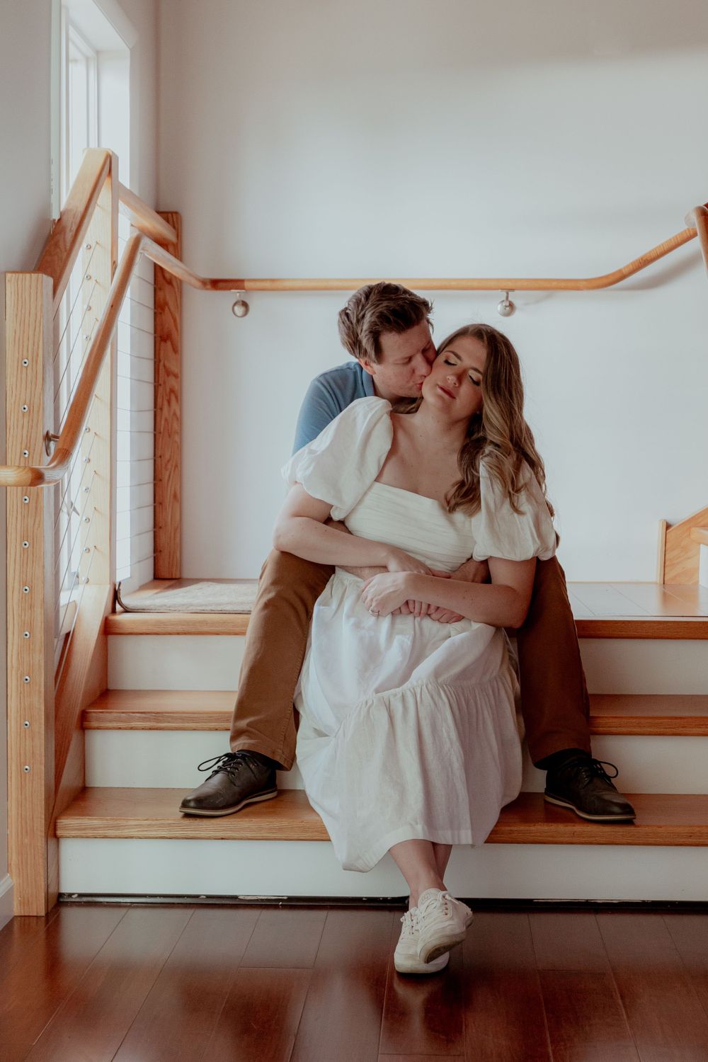 Couples photography: a couple sits on a wooden staircase with the man kissing the woman on the cheek and holding her