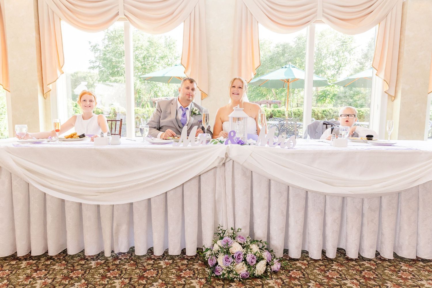 Wedding reception head table decorated with white linens and floral arrangements in an elegant ballroom.