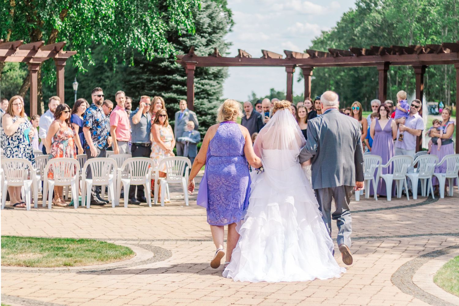 Wedding party walking down brick pathway after ceremony under wooden pergola.