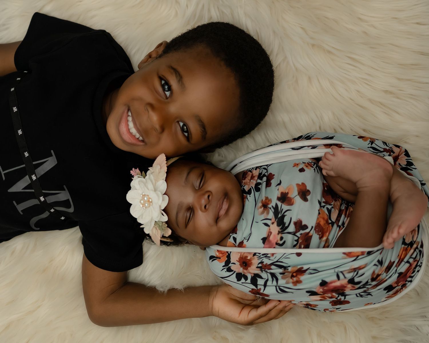 Two siblings share a sweet embrace while lying on plush white fur during a heartwarming photoshoot.