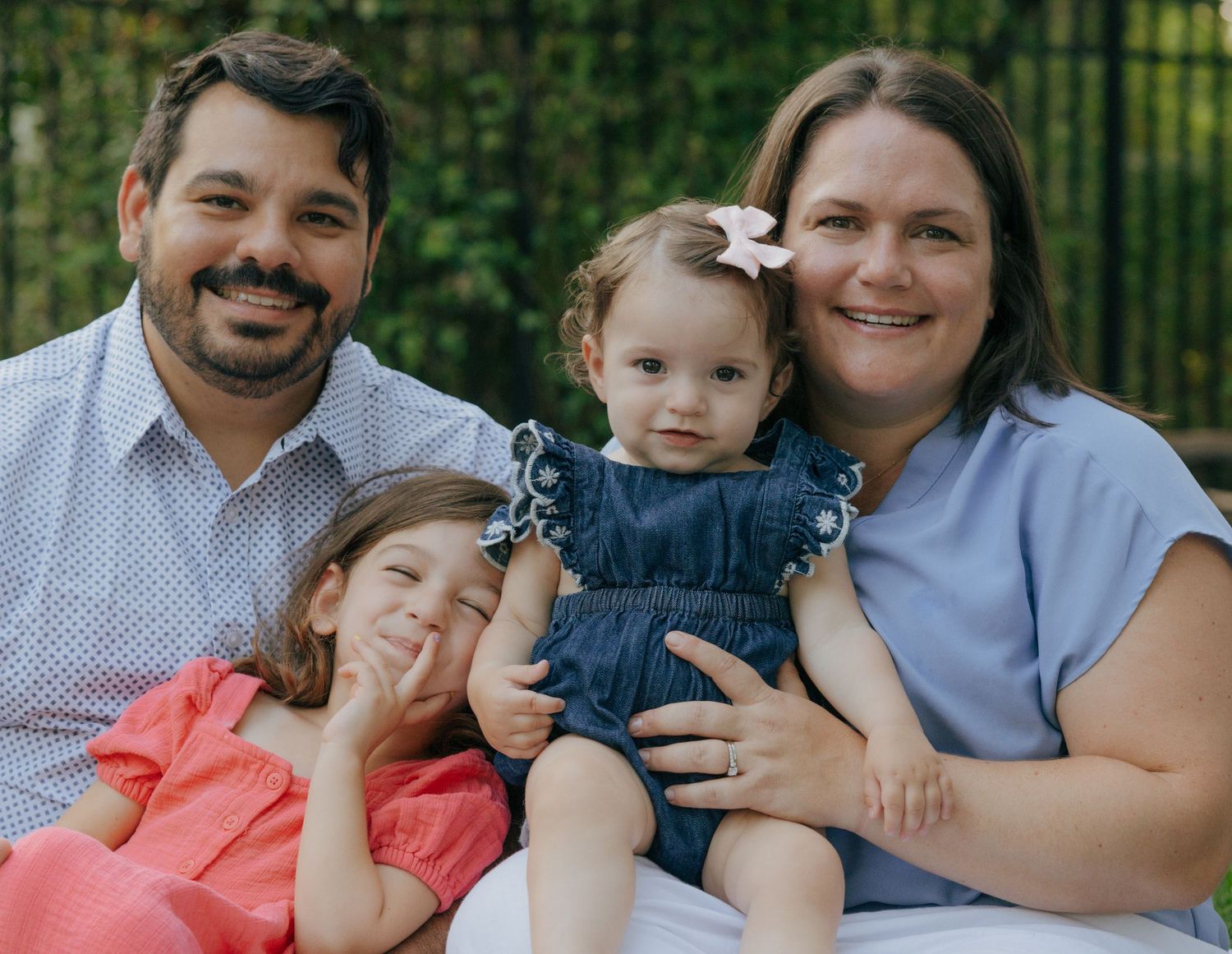 Family portrait outdoors with everyone smiling at camera on white blanket.