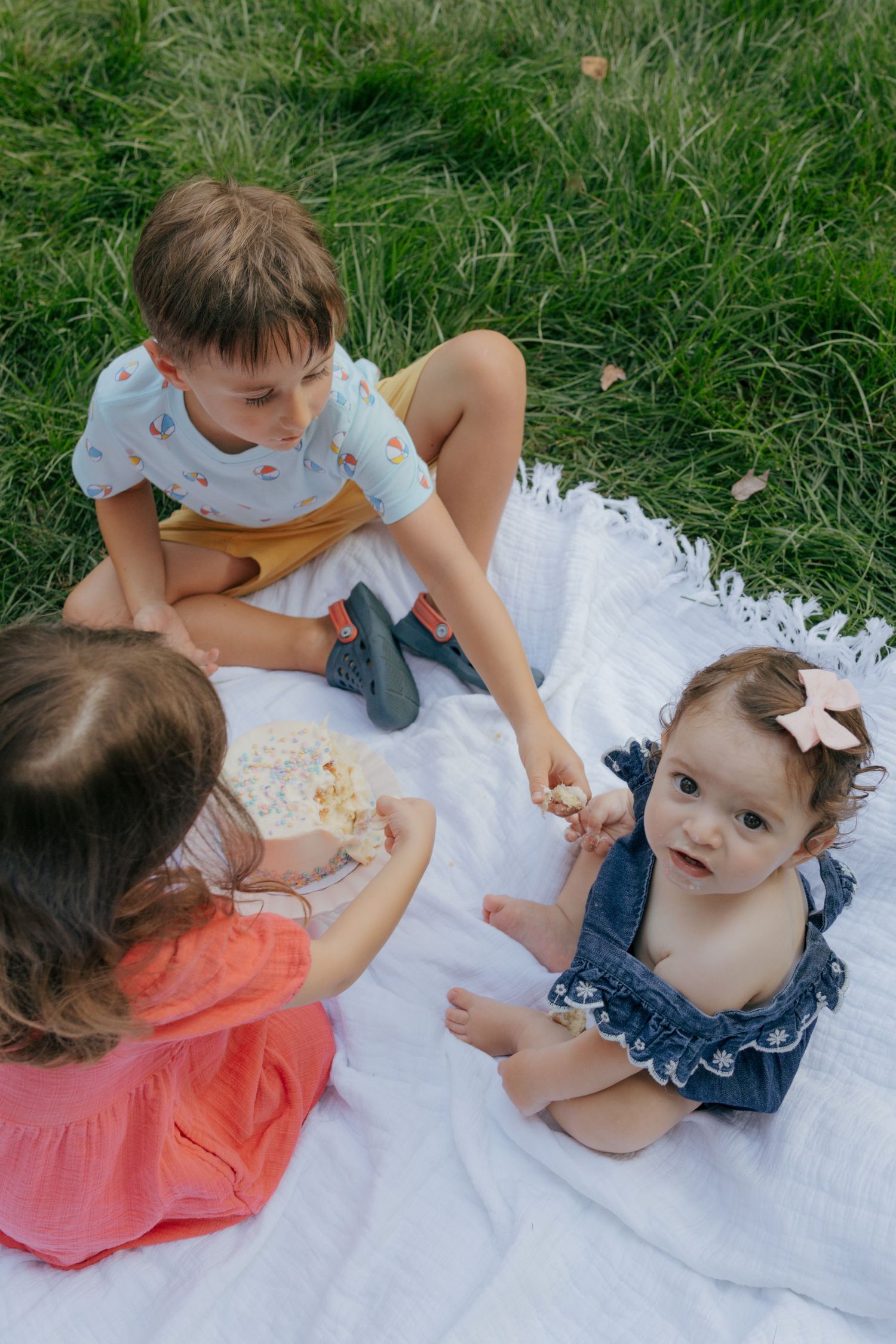 Children enjoying an outdoor picnic on a white blanket in the grass.
