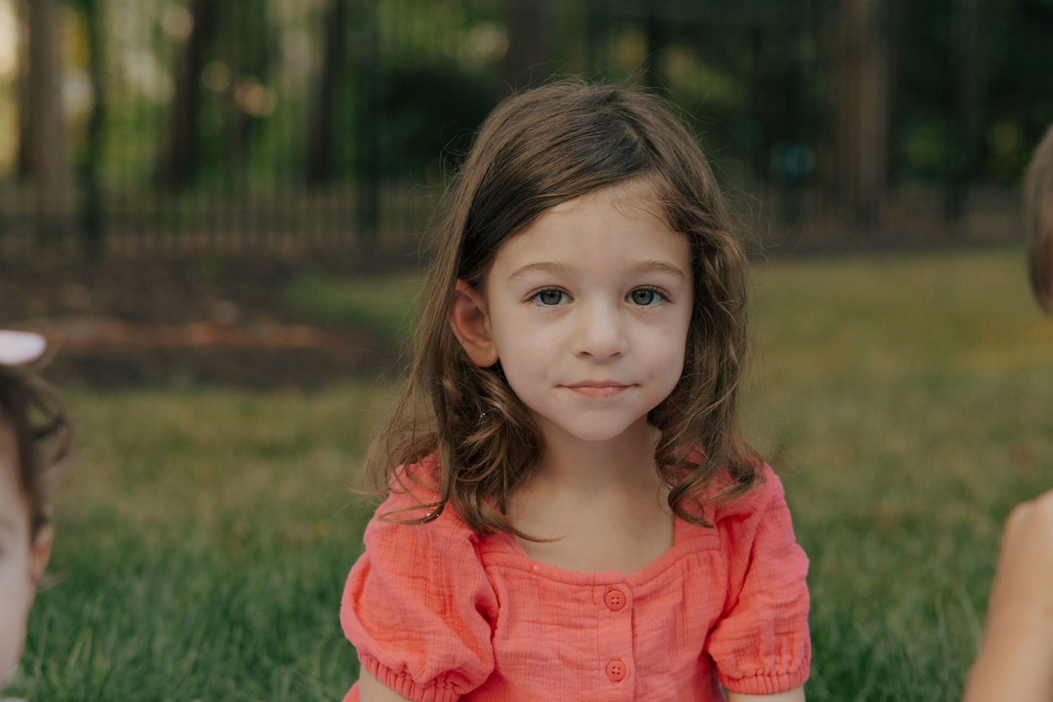Young person in a coral dress smiling outdoors on a sunny day.