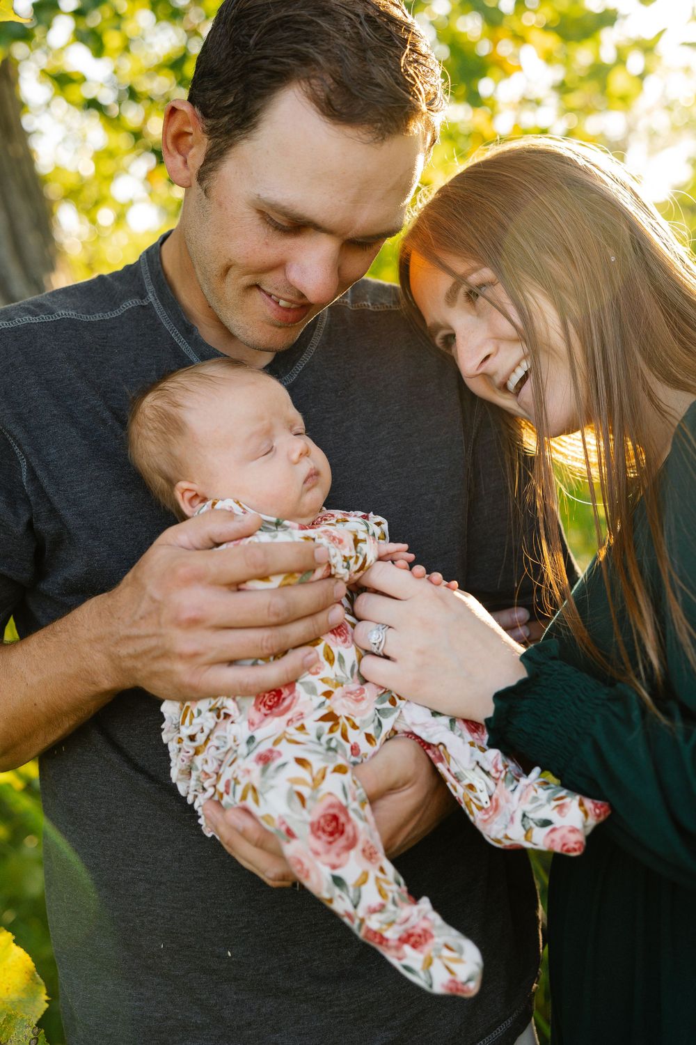 Parents share tender moments with their newborn baby outdoors in natural lighting.