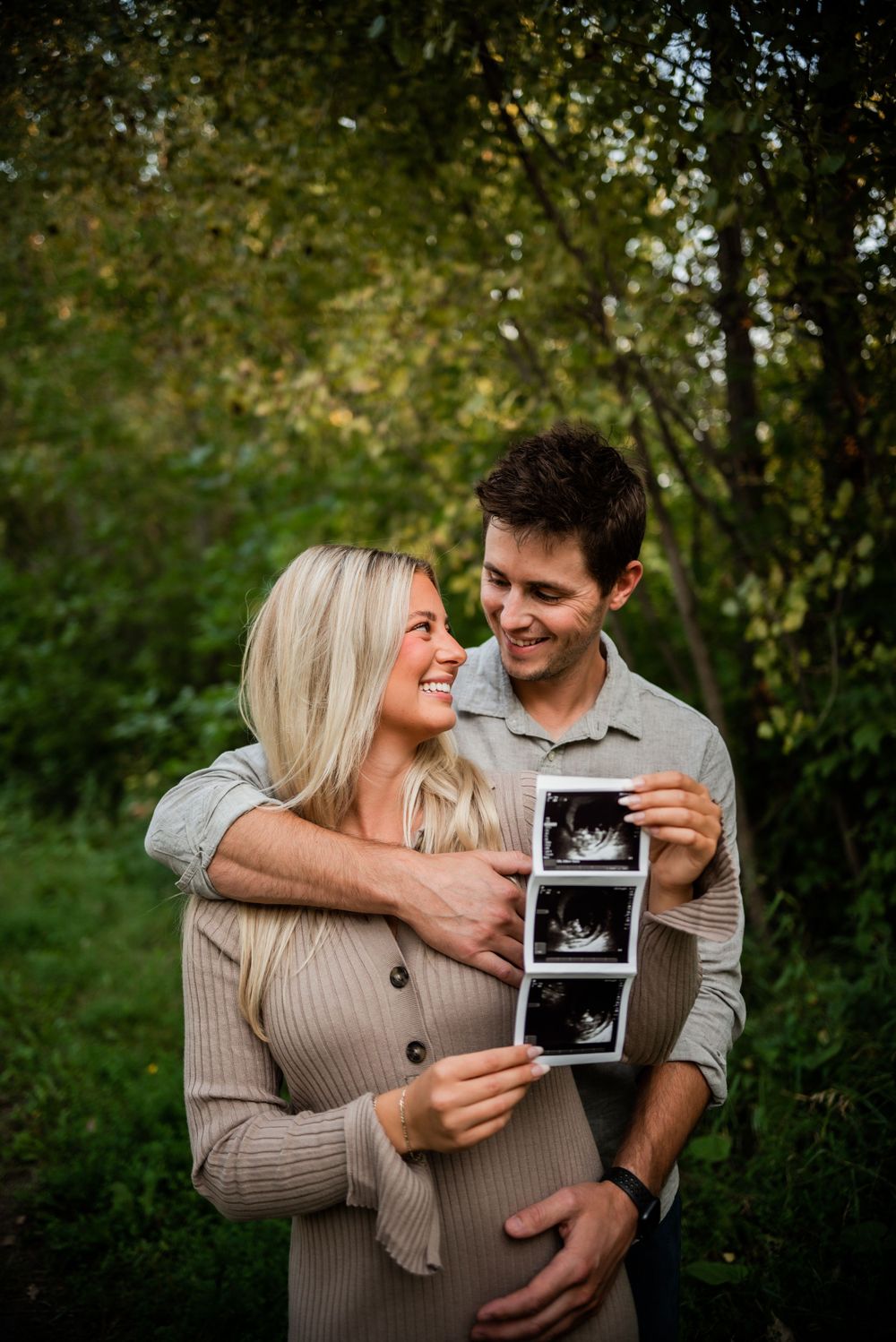 Couple sharing joyful moment while holding ultrasound photo in outdoor setting.