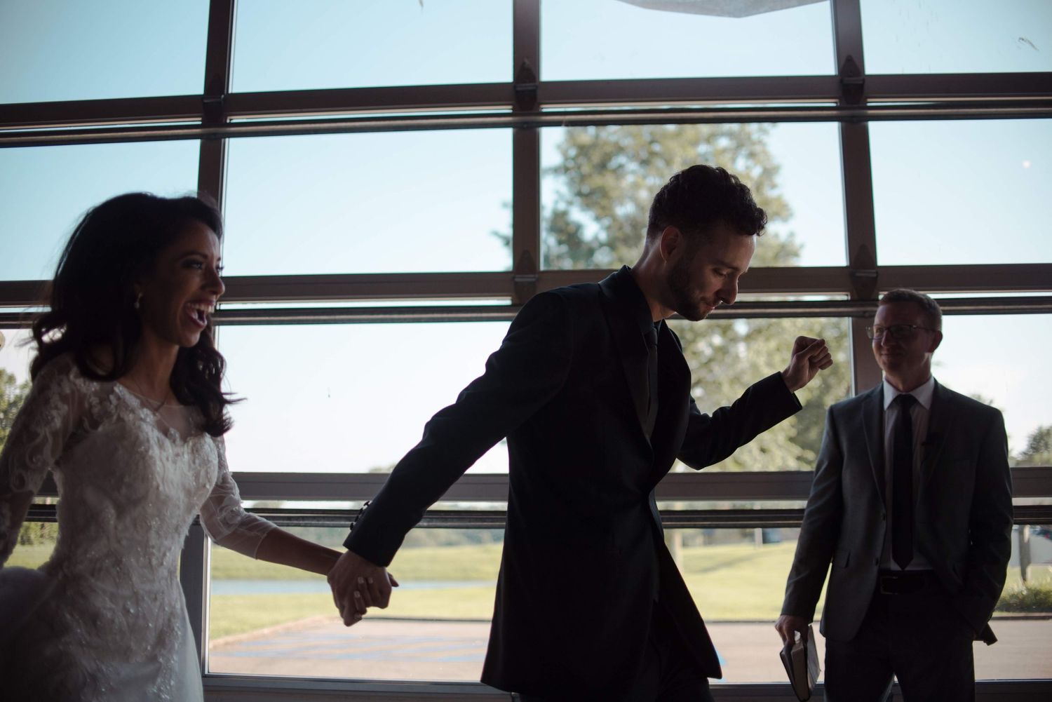 Silhouettes celebrate against large windows with natural backlighting in an indoor venue.