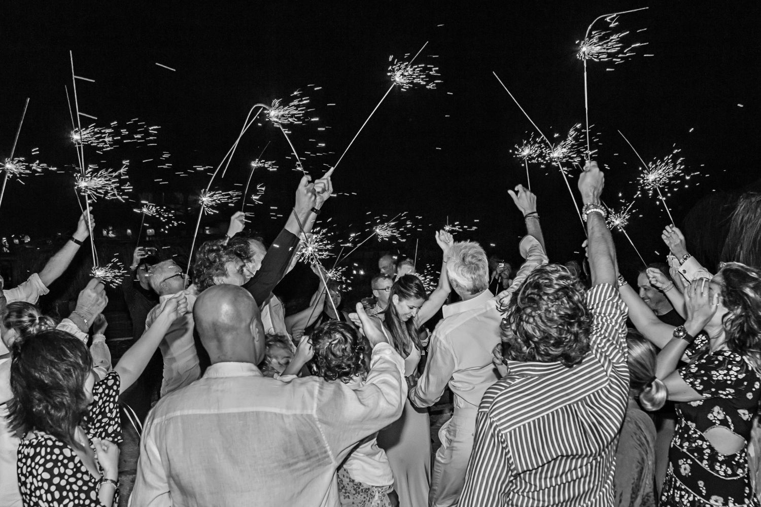 Wedding celebration with guests holding sparklers and dancing under the night sky.