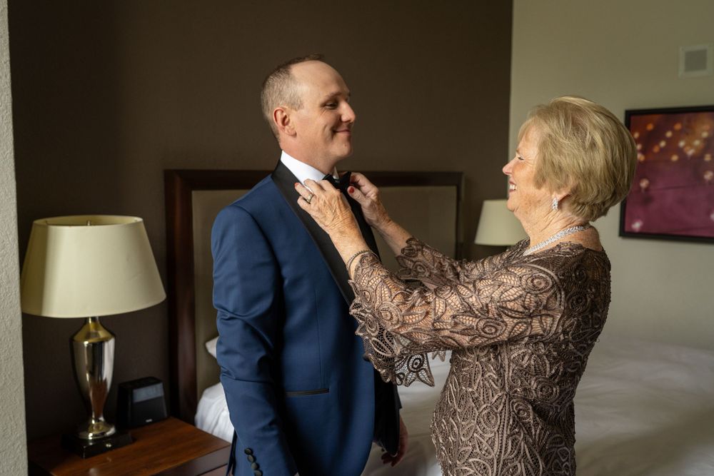 Mother adjusts grooms bow tie in hotel room before wedding ceremony.