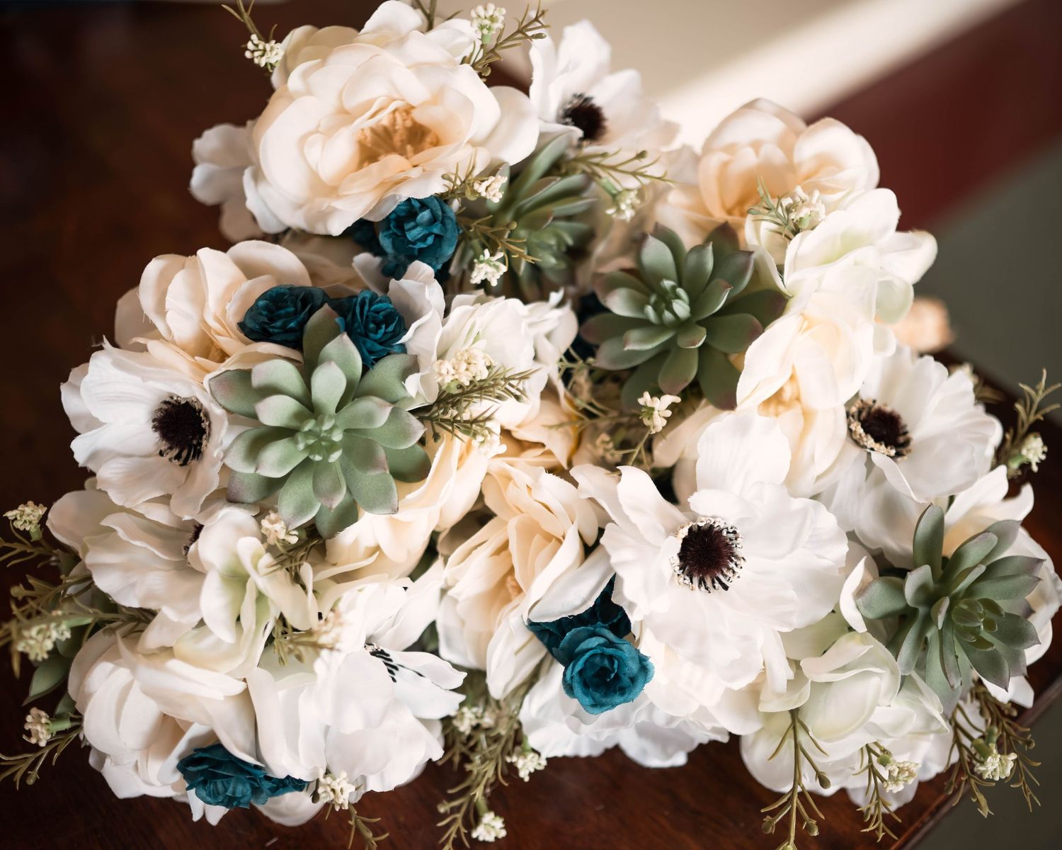 Wedding bouquet featuring white flowers, succulents, and teal accents arranged in an elegant design.