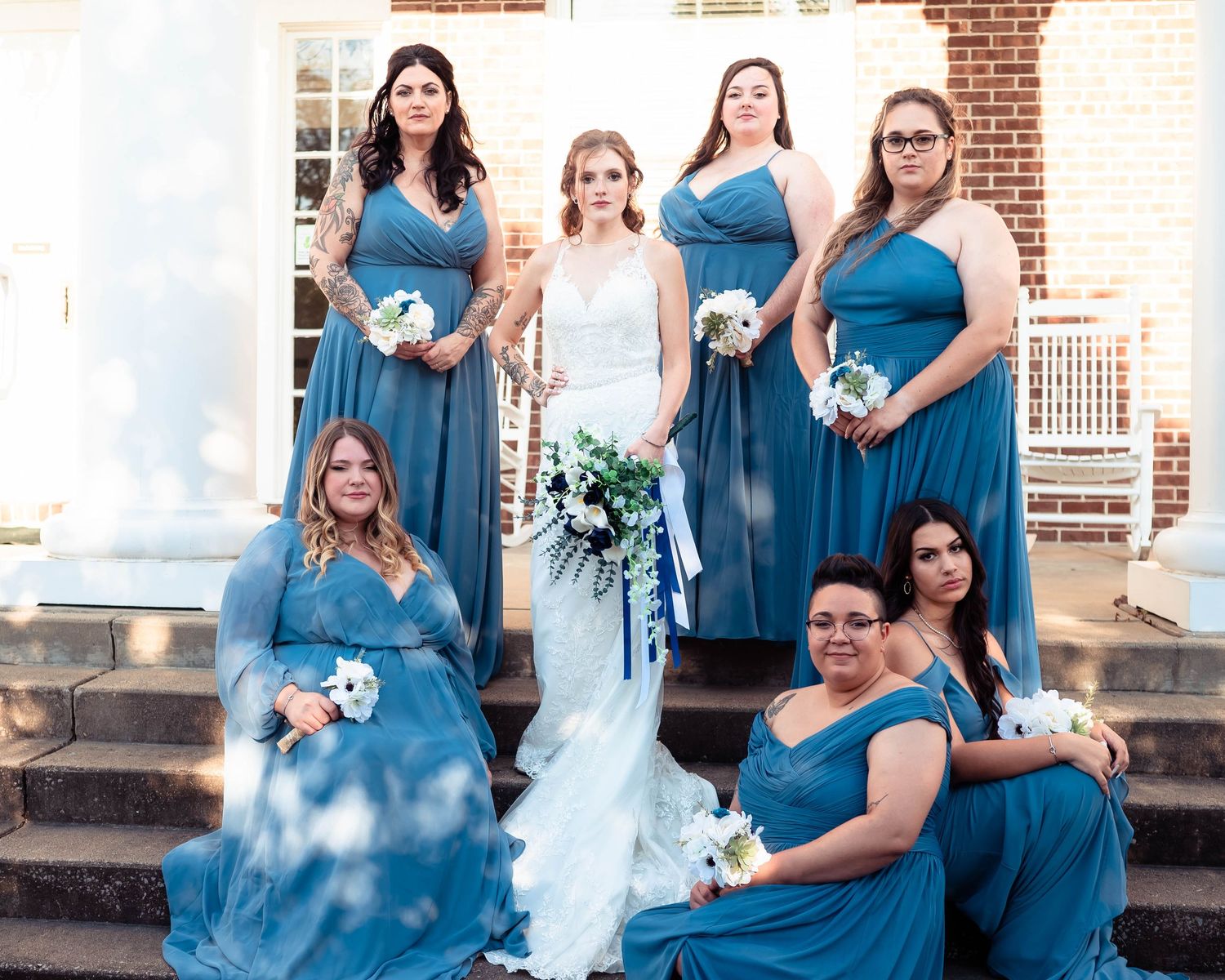 Wedding party in teal blue dresses poses together on brick steps for formal photos.