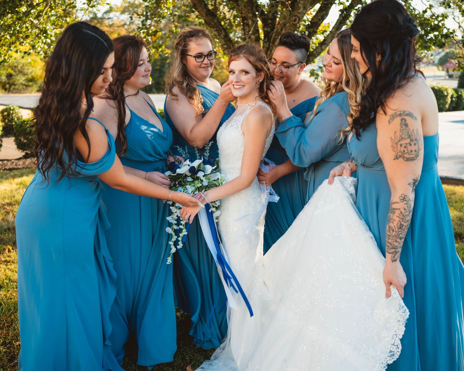 Wedding party in coordinated blue dresses gather for outdoor photos.