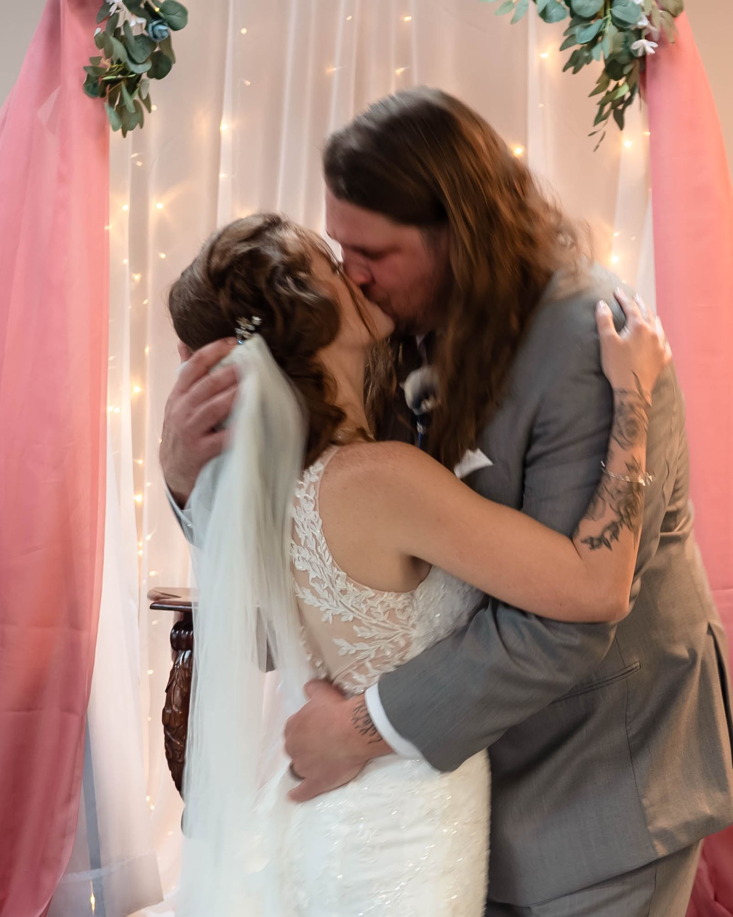 Romantic wedding kiss against pink backdrop with fairy lights.