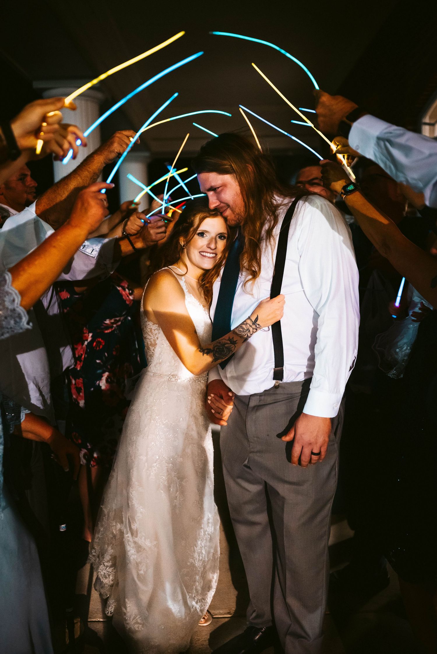 Wedding celebration with glow sticks creating light trails in dark reception venue.