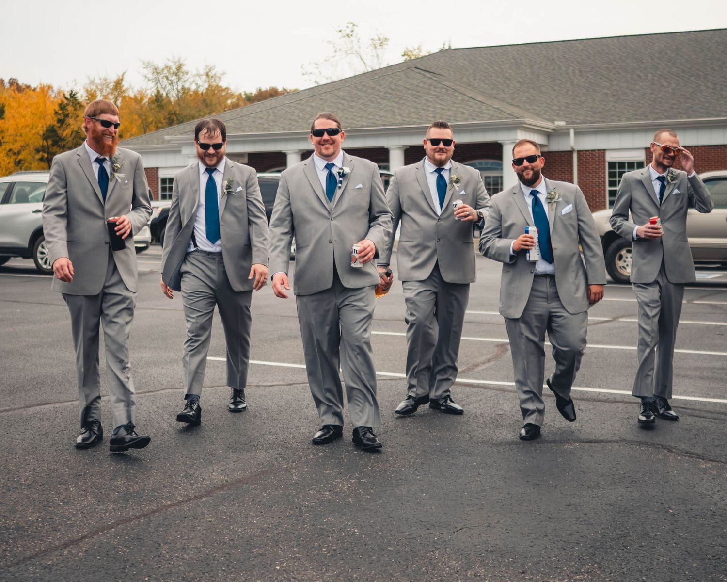 Groomsmen in grey suits perform synchronized dance moves in parking lot.