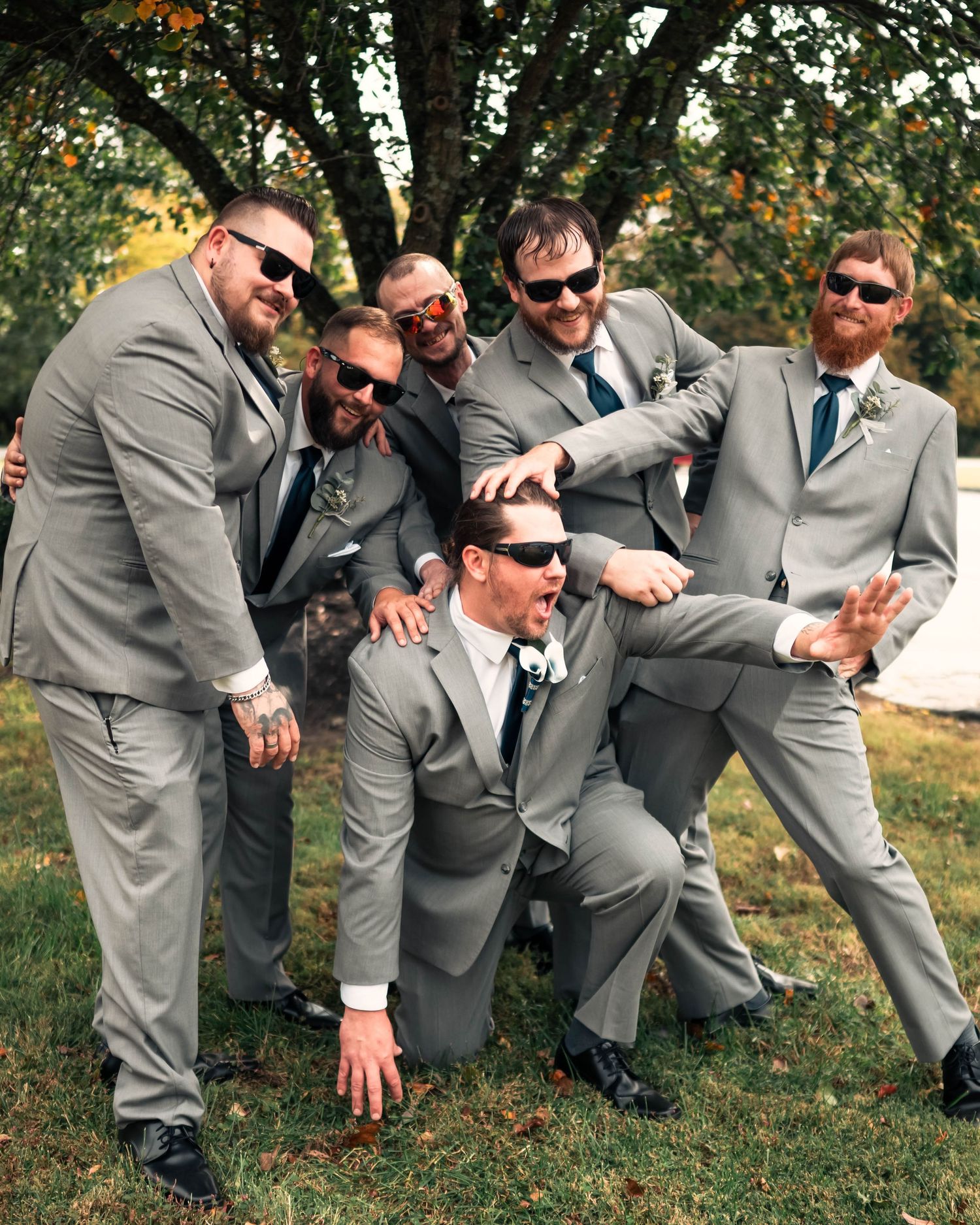 Wedding party in gray suits strike dynamic poses on grass during outdoor photo session.