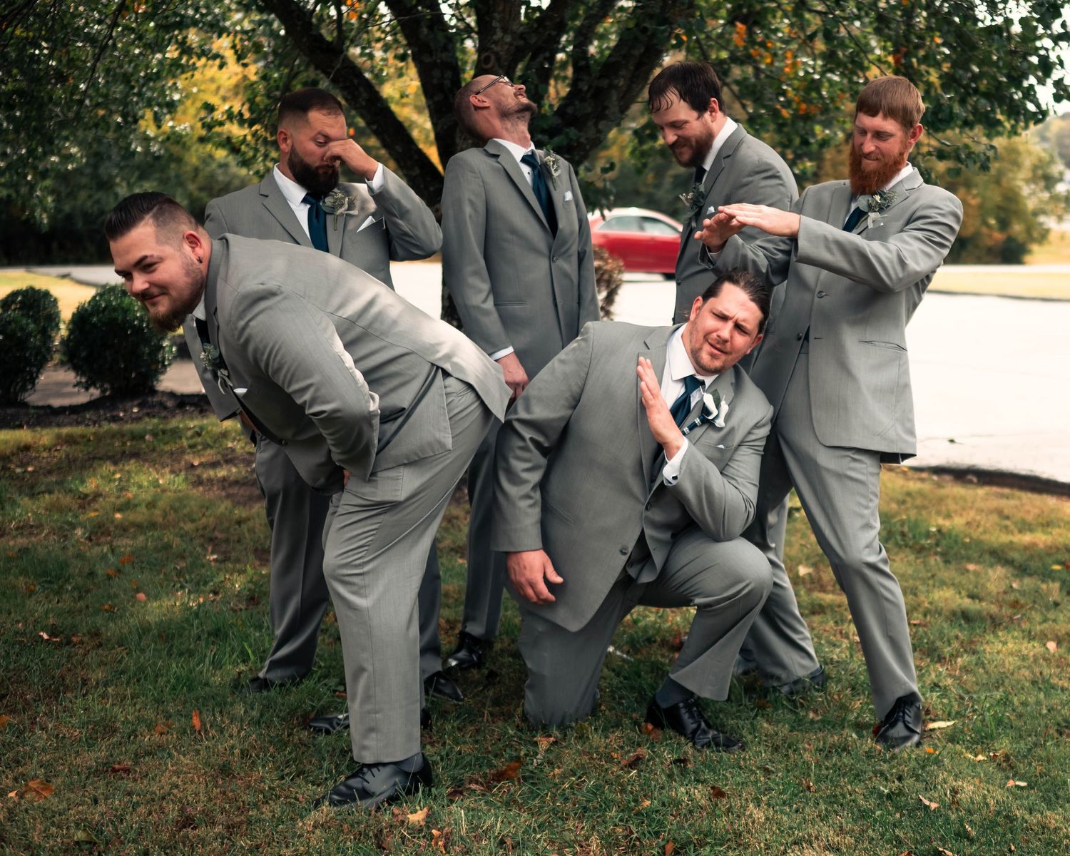 Groomsmen in gray suits perform a playful jumping pose outdoors during a wedding photoshoot.
