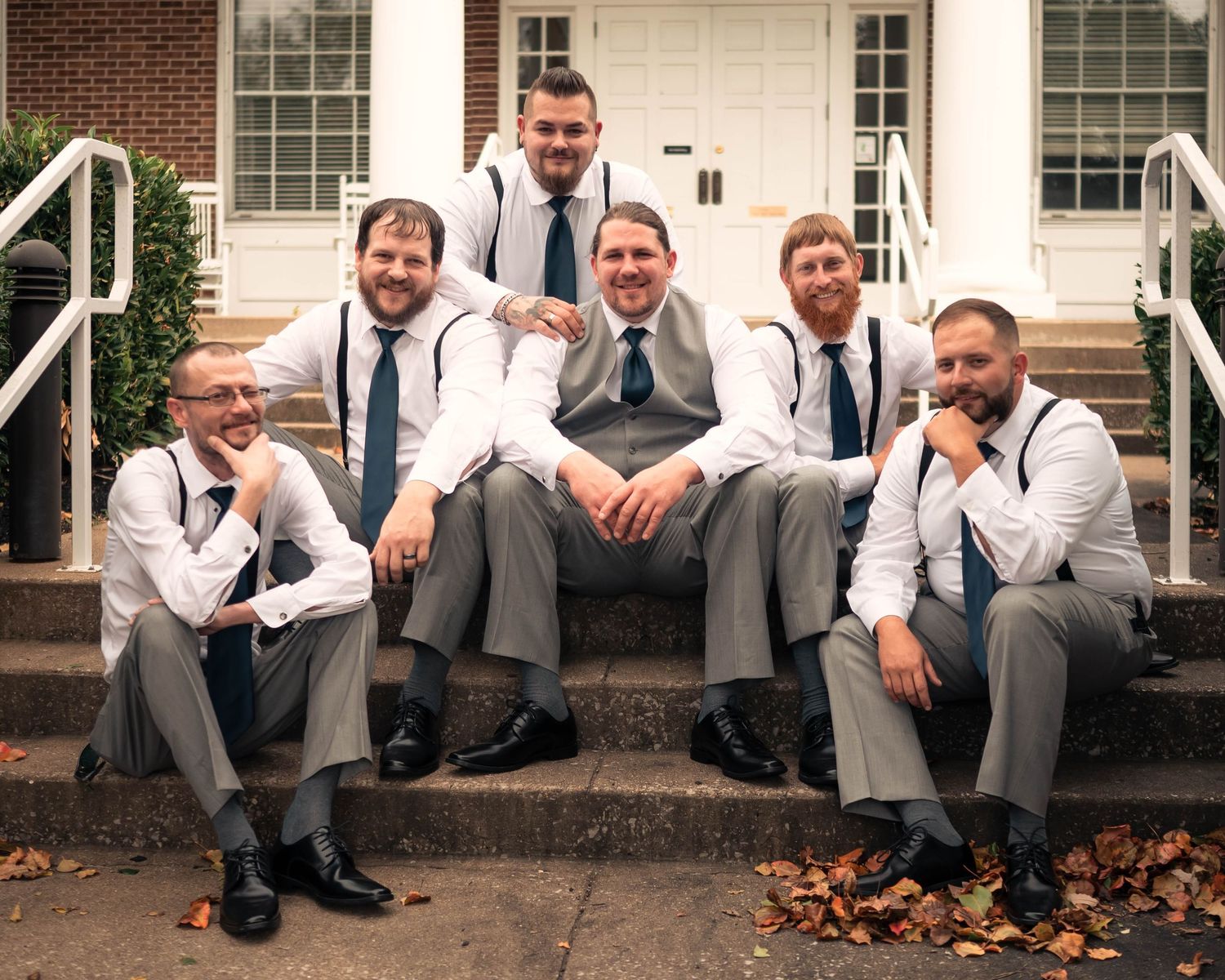 Wedding party members sit casually on brick steps for a relaxed group photo.
